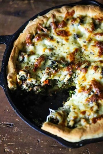 A deep dish pizza with sausage and broccoli in a cast-iron skillet with a slice cut out.