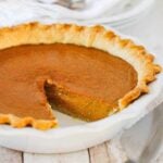 A pumpkin pie with a slice missing in a white pie dish.