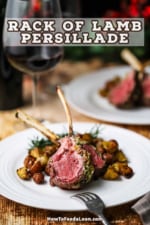 A close-up view of a white dinner plate filled with roasted potatoes topped with two medium-rare lamb chops all next to a glass of red wine.