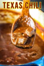 A wooden spoon holding up a spoonful of authentic Texas chili.