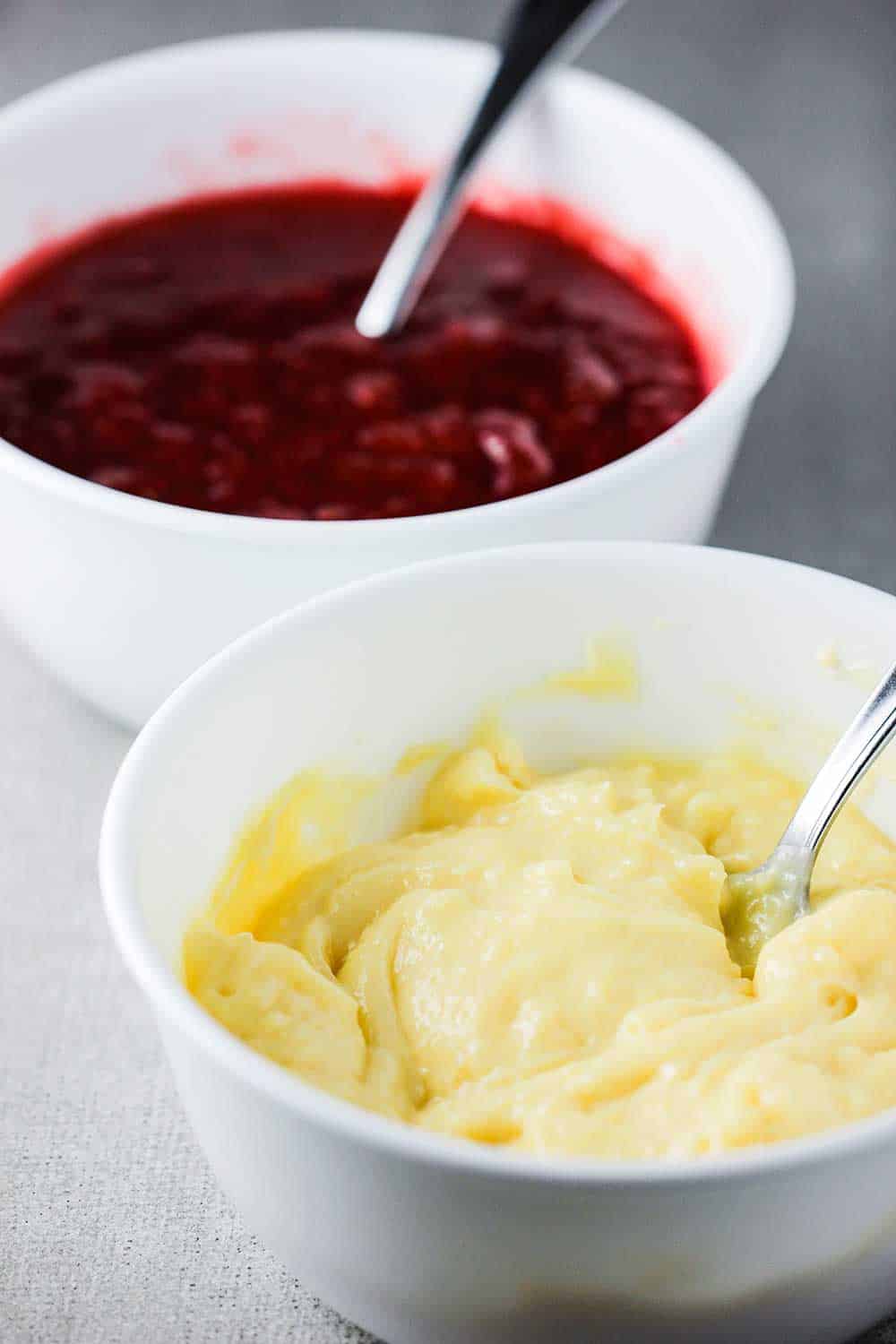 Two white bowls, one filled with strawberry jelly and the other with vanilla custard.
