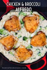An overhead view of a large red skillet holding seared chicken thighs in a broccoli and pasta alfredo sauce.