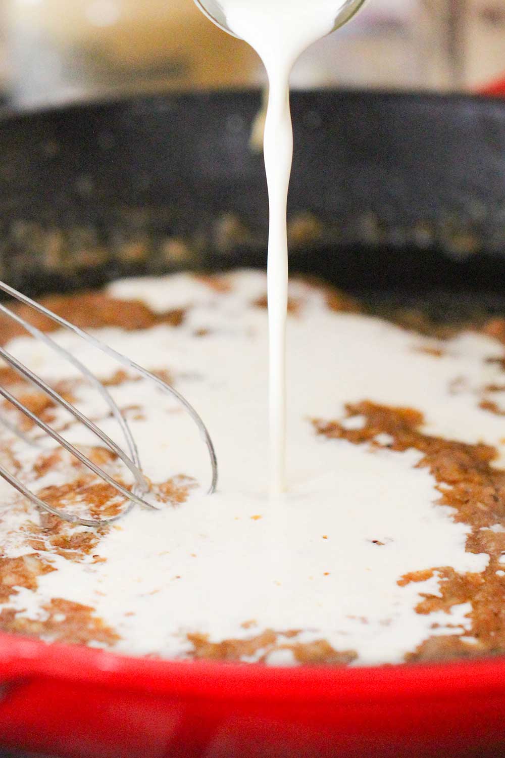 Cream being poured into a red skillet with a roux in it.