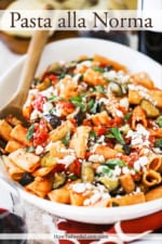 A large white oval serving platter filled with a tomato pasta topped with cooked eggplant pieces and crumbled cheese.
