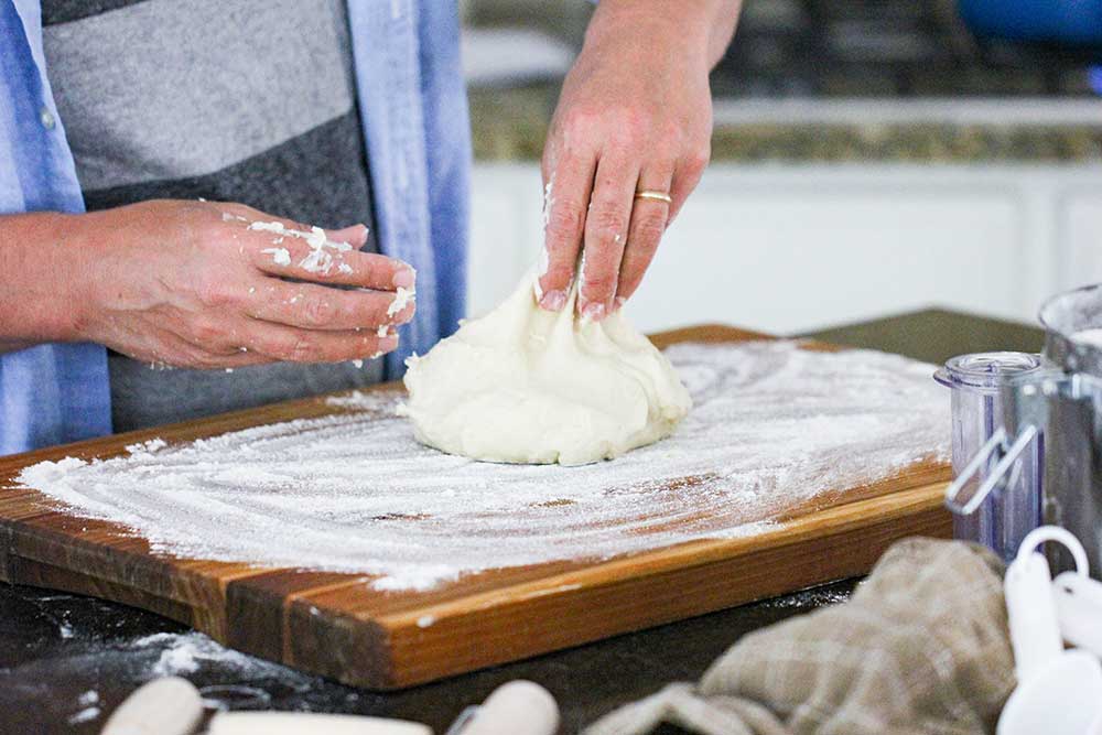 A cook pulling a piece of flour tortilla dough on a floured cutting board.