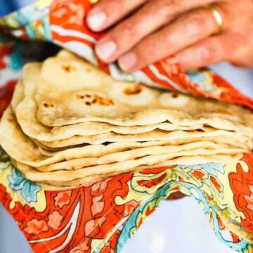 Hands holding a stack of homemade flour tortillas in a colorful cloth.