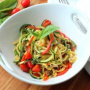 A white serving bowl filled with spiralized ratatouille next to a white napkin.