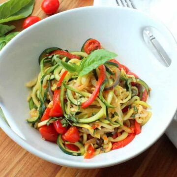 A white serving bowl filled with spiralized ratatouille next to a white napkin.