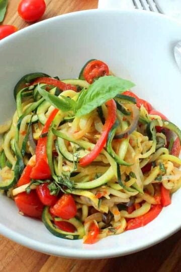 A white serving bowl filled with spiralized ratatouille next to a white napkin.