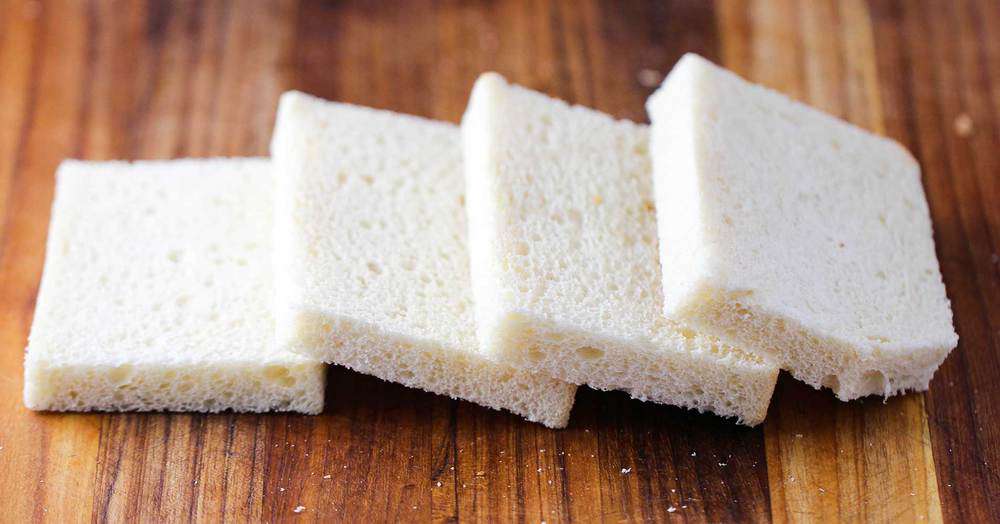4 slices of day-old bread with crusts removed on a cutting board.