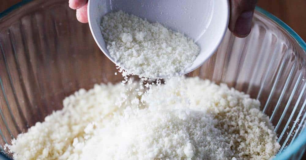 Fresh bread crumbs with Parmesan cheese being pour into a clear bowl.