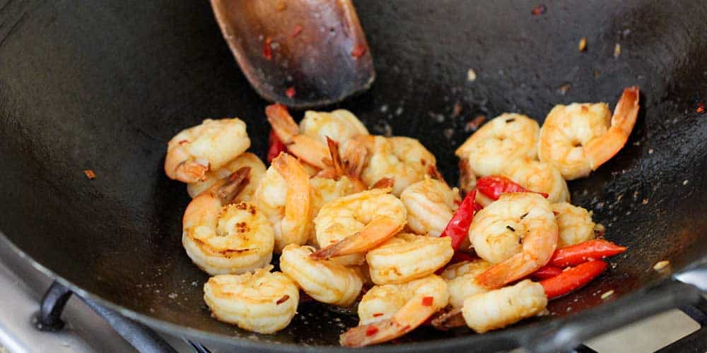 Shrimp being stir-fried in a wok for authentic shrimp pad Thai.