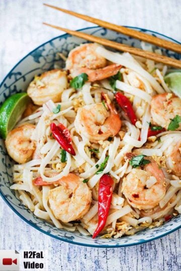 An overhead view of a colorful bowl filled with shrimp pad Thai with two chop sticks on the side of the bowl.
