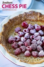 A whole chess pie topped with fresh raspberries and sprinkled with powdered sugar.