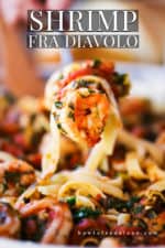 A hand lifting up a fork filled with shrimp fra diavalo from a bowl of the same.