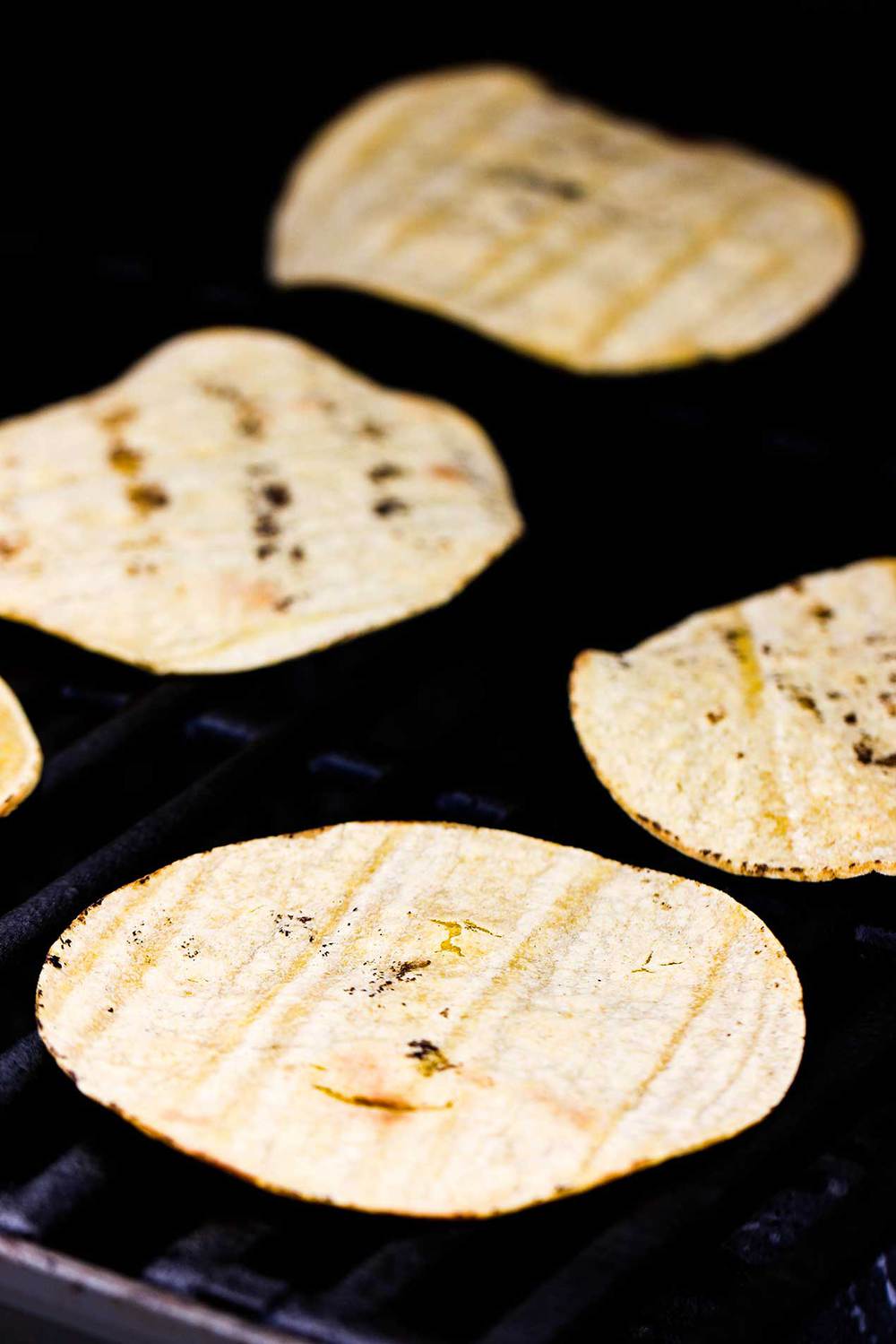 Corn tortillas heating up on a gas grill.