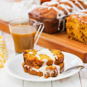 Two slices of pumpkin butterscotch bread on a white plate next to a cup of coffee.