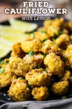 A close-up view of a black plate filled with a pile of fried cauliflower topped with chopped parsley and coarse sea salt.