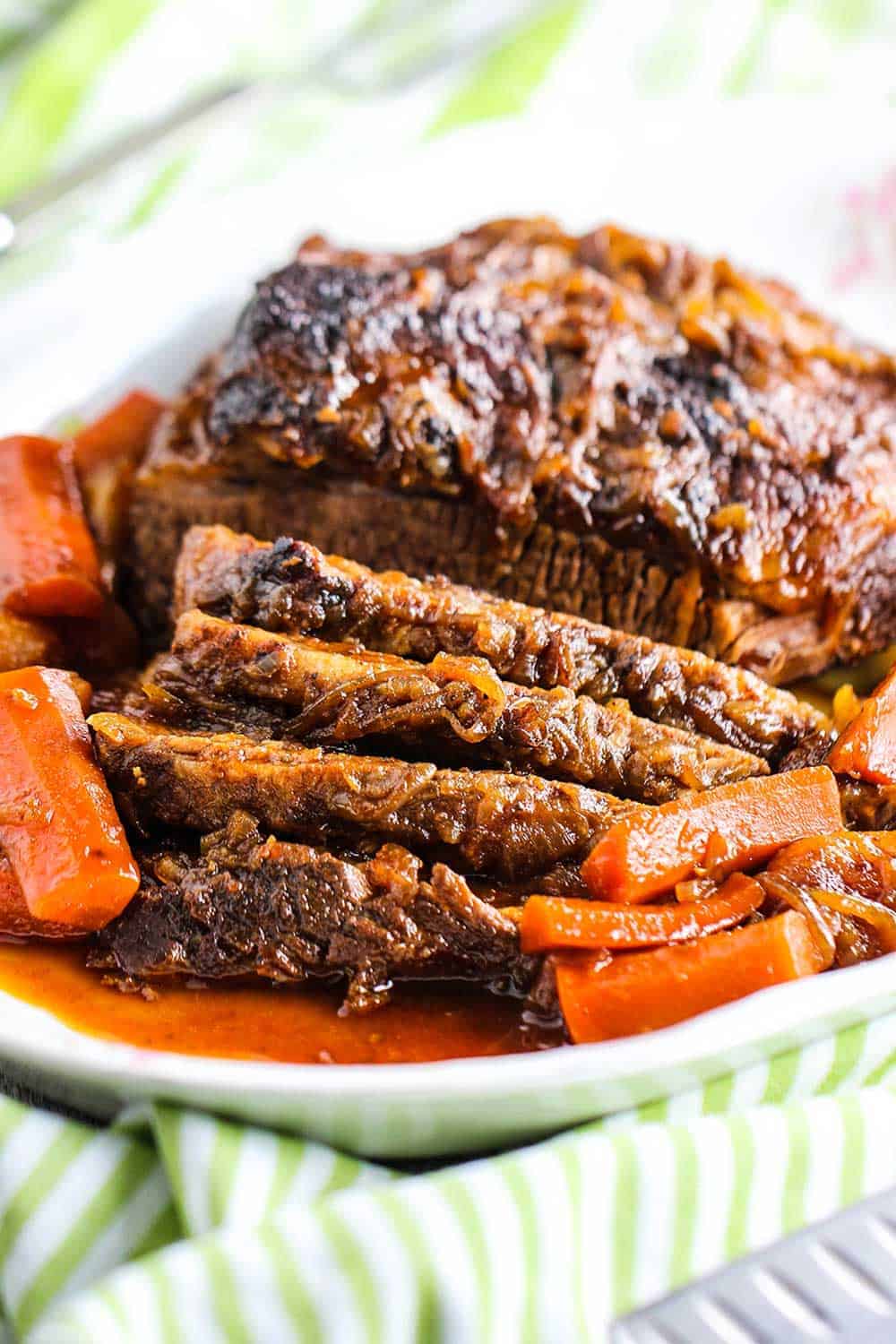 A sliced beef brisket on a large platter with a patterned napkin next to it. 
