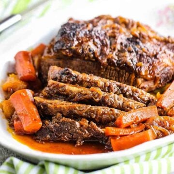 A sliced beef brisket on a large platter with a patterned napkin next to it.