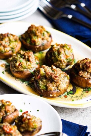 A platter filled with sausage-stuffed mushrooms next to a plate of the same.