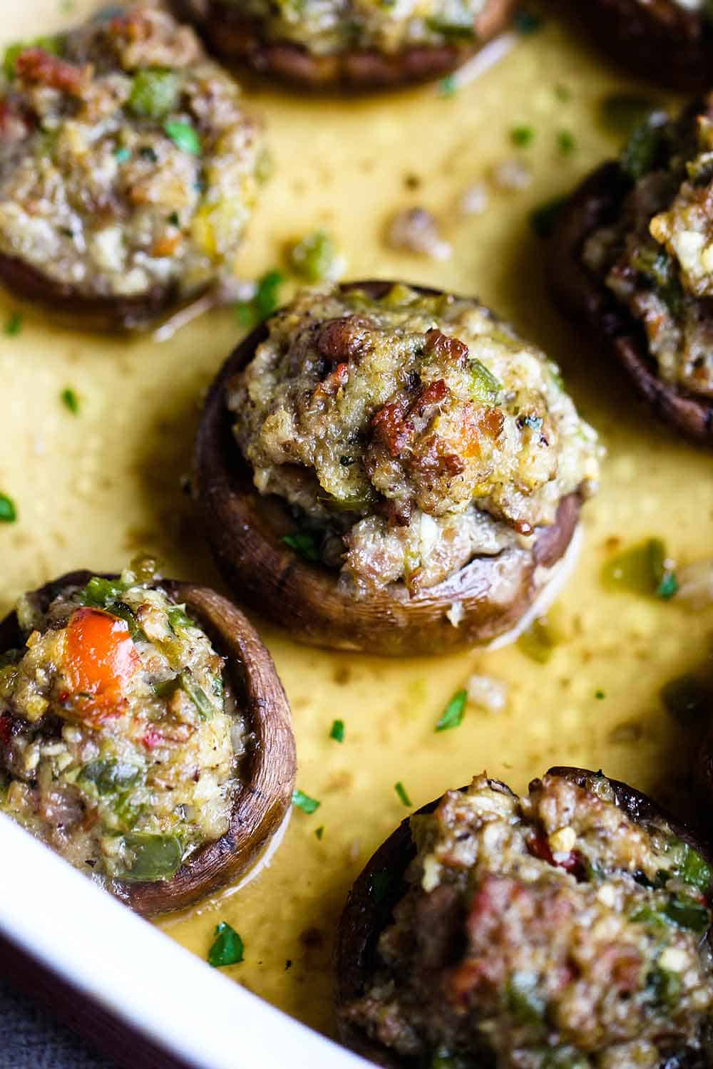A baking dish filled with sausage-stuffed mushrooms sitting in chicken stock.