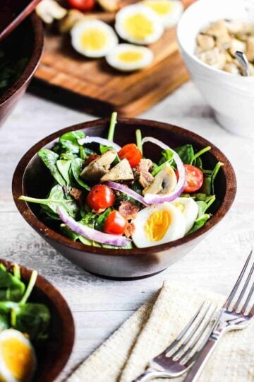Warm Spinach and Bacon Salad in a bowl next to two forks on top of a beige napkin