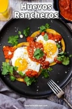 An overhead view of a black plate holding a serving of huevos rancheros sitting next to a glass of orange juice.