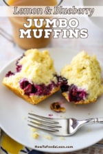 A straight-on view of a lemon blueberry muffin that has been split in half on a small white plate sitting next to a glass mug full of coffee.