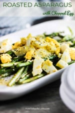 An oval white platter filled with roasted asparagus topped with chopped hard-boiled eggs.