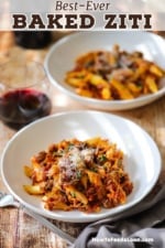 Two white pasta bowls filled with a dinner-sized portion of baked ziti topped with grated Parmesan cheese and sitting next to a stemless glass of red wine.