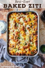 An overhead view of a lasagna pan filled with an undisturbed pan of baked ziti with glasses of red wine nearby.