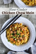 An overhead view of a grey bowl filled with slow-cooker chicken chow mein flanked by two black chopsticks.