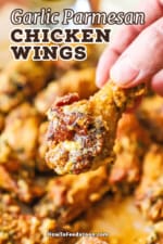 A person holding a garlic Parmesan chicken wing over a pile of the same wings.