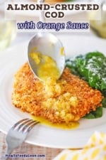 A dinner spoon being used to drizzle an orange shallot sauce over an almond crusted fillet of cod next to a spinach salad.