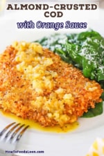 A close-up view of an almond crusted cod with orange sauce next to a small pile of a spinach salad on a white dinner plate.
