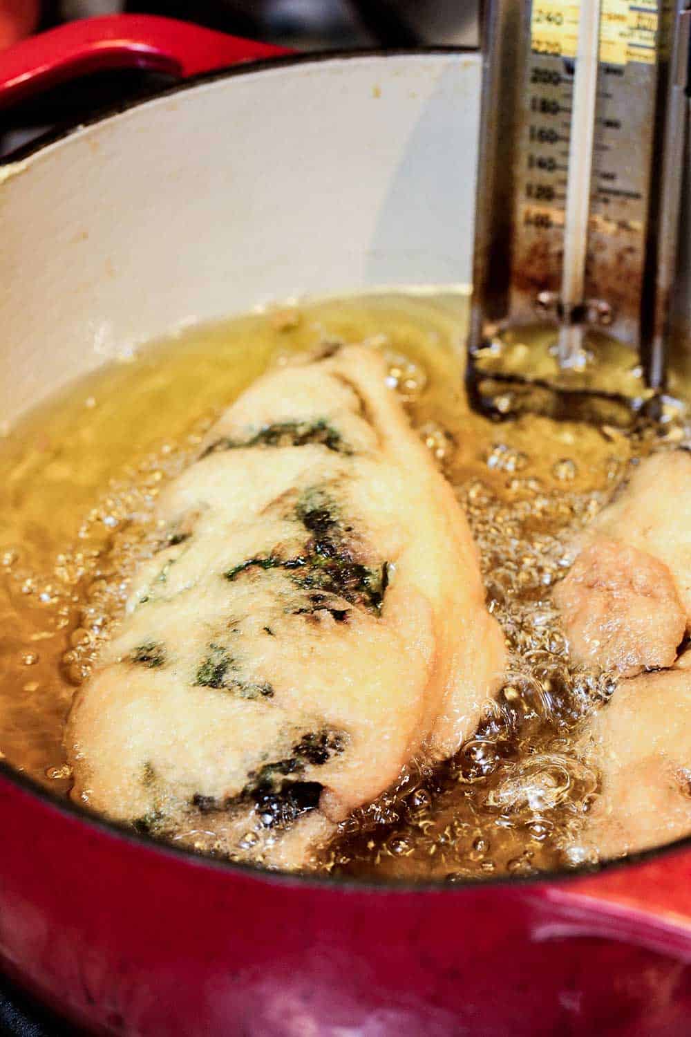 A chile relents frying in a large pot of hot oil.