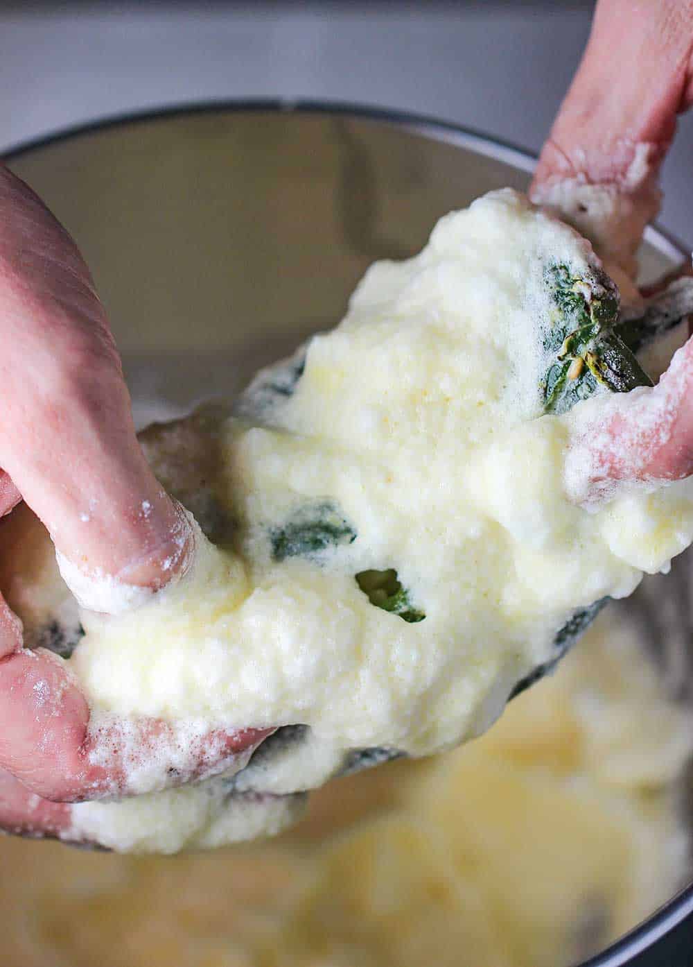 Two hands holding a pabloano pepper that has been dipped in batter.