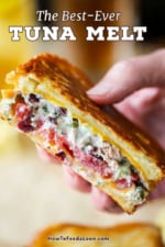 A close-up view of a person holding up a tuna melt sandwich that has been sliced in half.