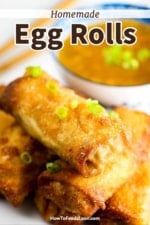 A stack of fried egg rolls on a white platter next to a bowl filled with duck sauce and topped with chopped scallions.