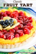 A close-up view of a fruit tart that it topped with concentric circles of mango, strawberries, kiwi, and blueberries.