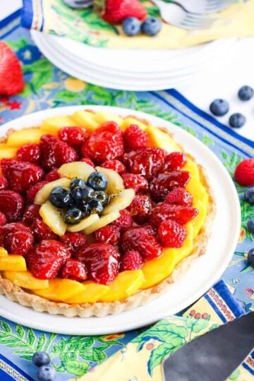 An overhead view of a summer fruit tart that is sitting on a circular white serving plate.