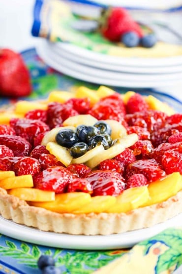 A close-up view of a summer fruit tart next to a stack of dessert plates.