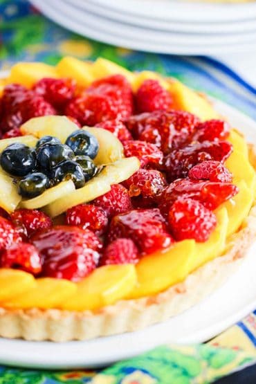 A close-up view of a fruit tart that has layers of sliced mango, strawberries, kiwi, and blueberries.
