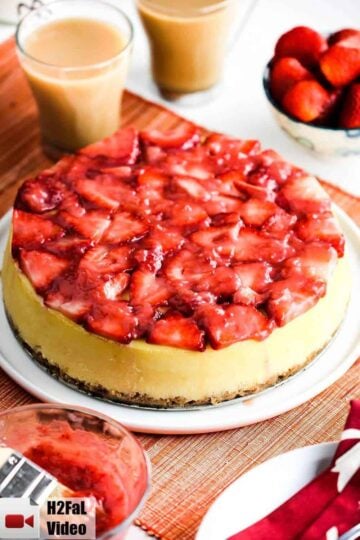 New York Style Cheesecake with strawberry glaze on a white plate with a cup off coffee.