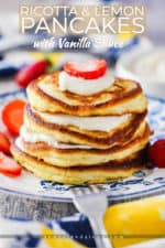 A stack of ricotta lemon pancakes on an antique plate with strawberries and a fork nearby.