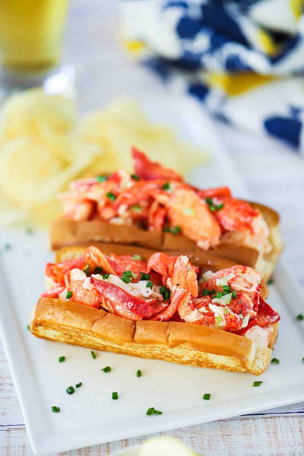 Two lobster rolls sitting on a rectangular white plate with snipped chives sprinkled over the top.