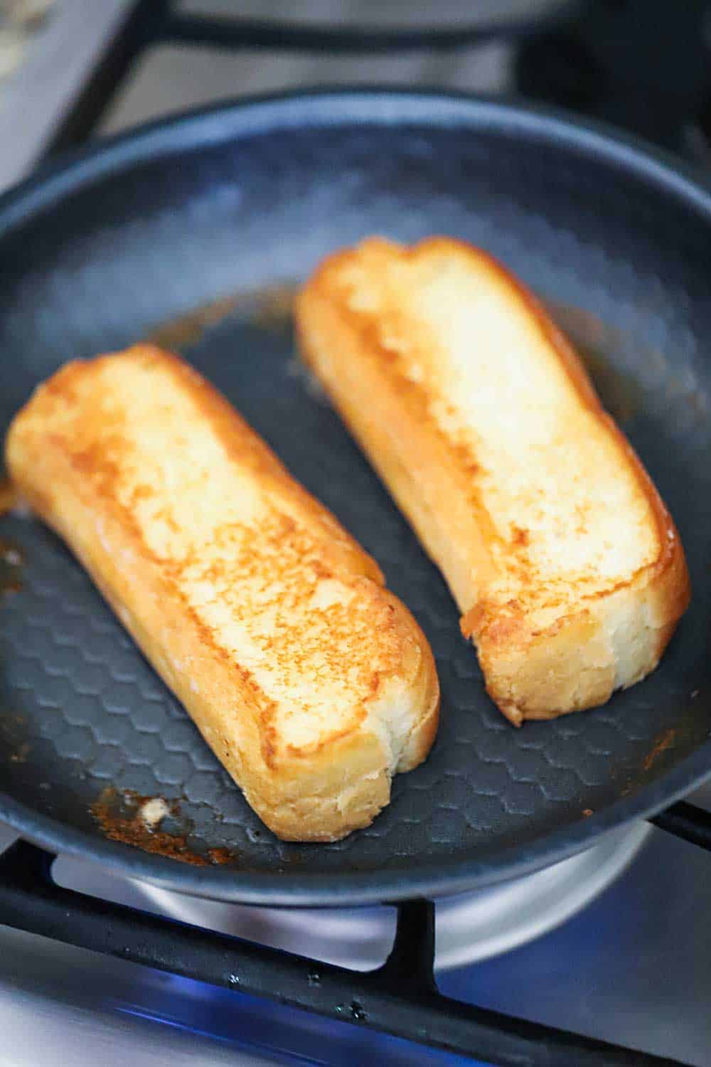 Two New England split-top buns that have been grilled and toasted in a small non-stick skillet.