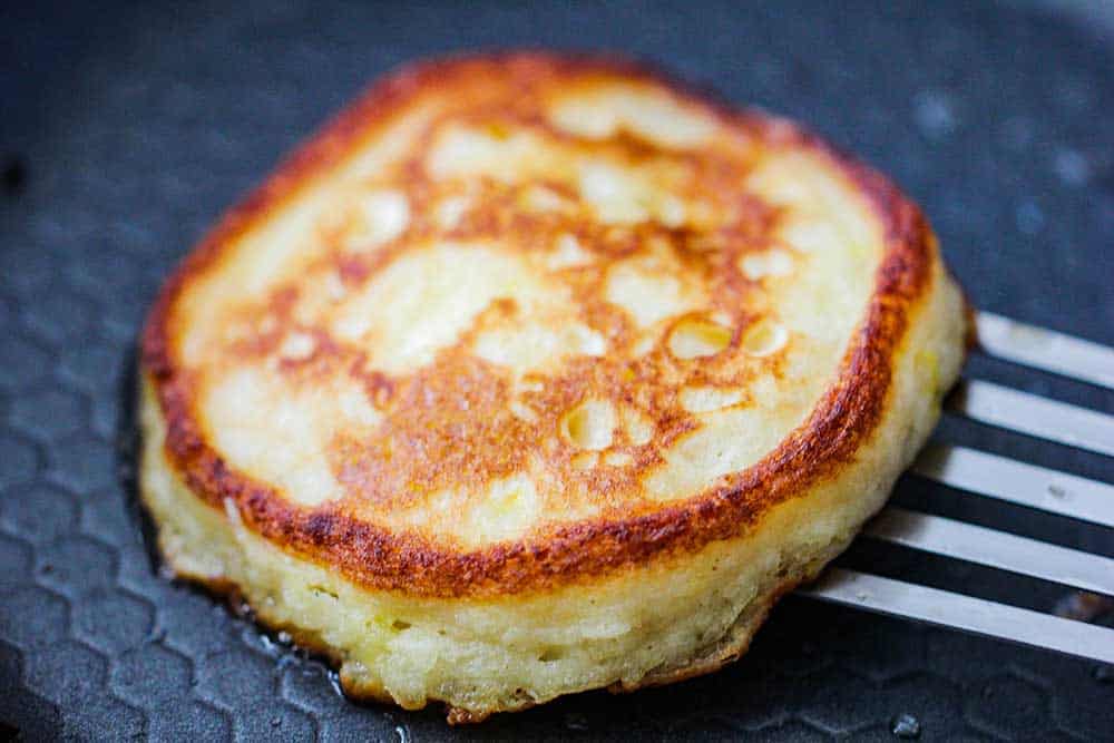 A perfectly cooked ricotta lemon pancake in a skillet with a spatula underneath it.