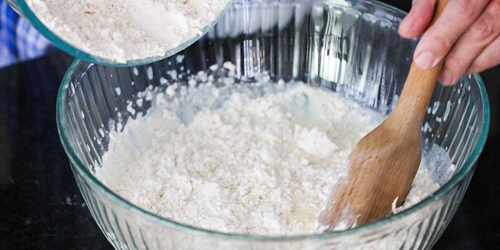 A wooden spoon mixing in a dry mixture into a wet mixture for ricotta lemon pancakes.